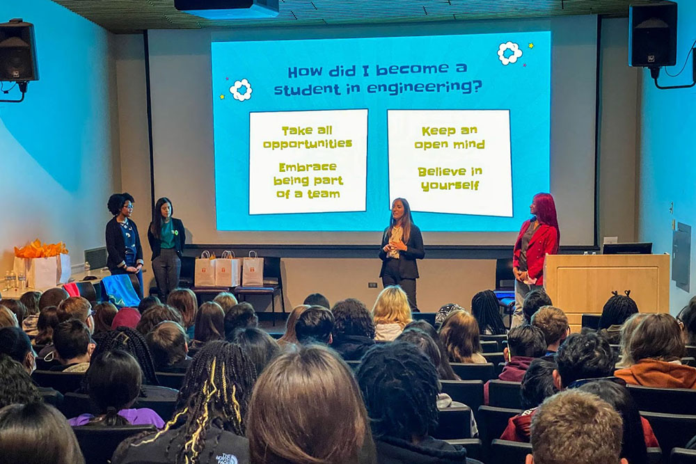 Four women speak to a crowd with a screen behind them that reads "How did I become a student in engineering?"